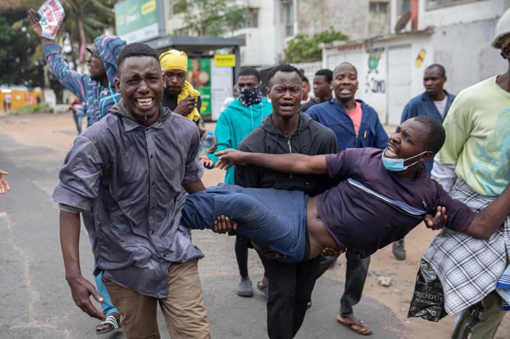 Manifestantes carregam um manifestante ferido por uma bala de borracha disparada pela polícia de choque em Maputo, a 7 de novembro de 2024. A polícia disparou gás lacrimogéneo para dispersar os manifestantes reunidos depois de o principal líder da oposição ter convocado uma manifestação sobre os resultados eleitorais. Foto de ALFREDO ZUNIGA/AFP via Getty Images